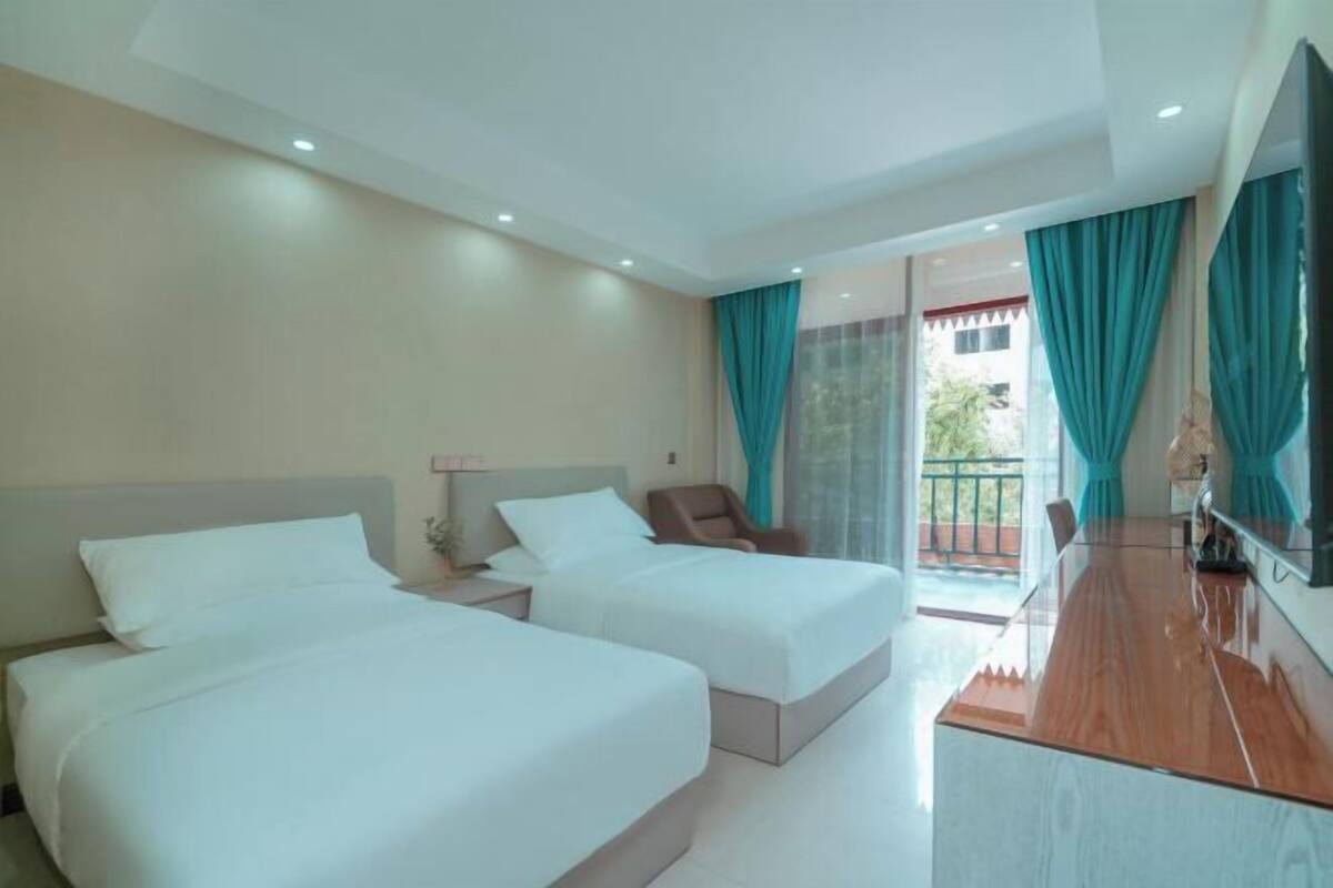 Une chambre d’hôtel avec deux lits, un bureau, une chaise et un balcon avec des rideaux.