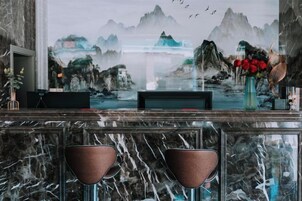 Uma área de bar com bancada de mármore, dois bancos altos, uma televisão e um vaso decorativo com flores.