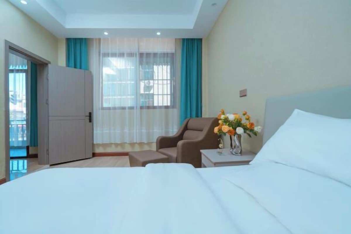 Una habitación de hotel con una cama, una silla, una mesita con un florero y un armario.