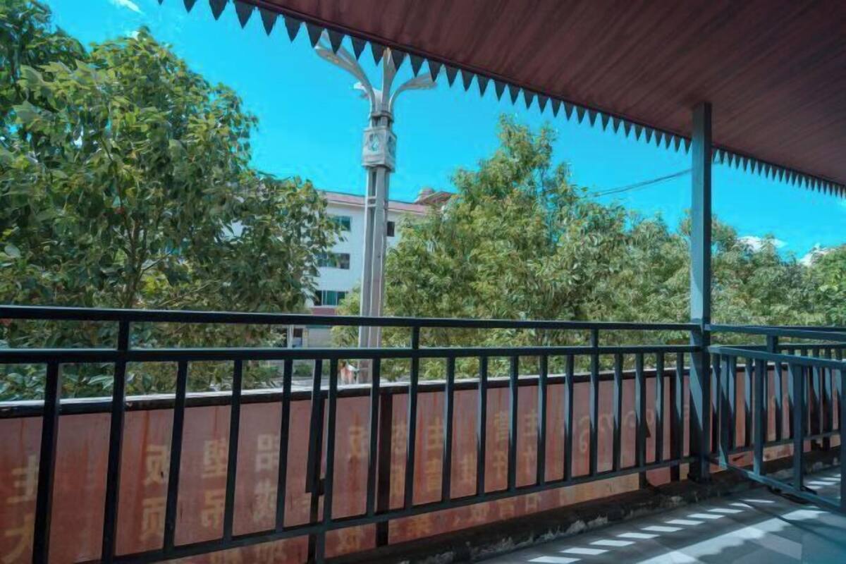 Un espace extérieur abrité, doté d’une rambarde en métal, d’arbres et d’un bâtiment en arrière-plan.