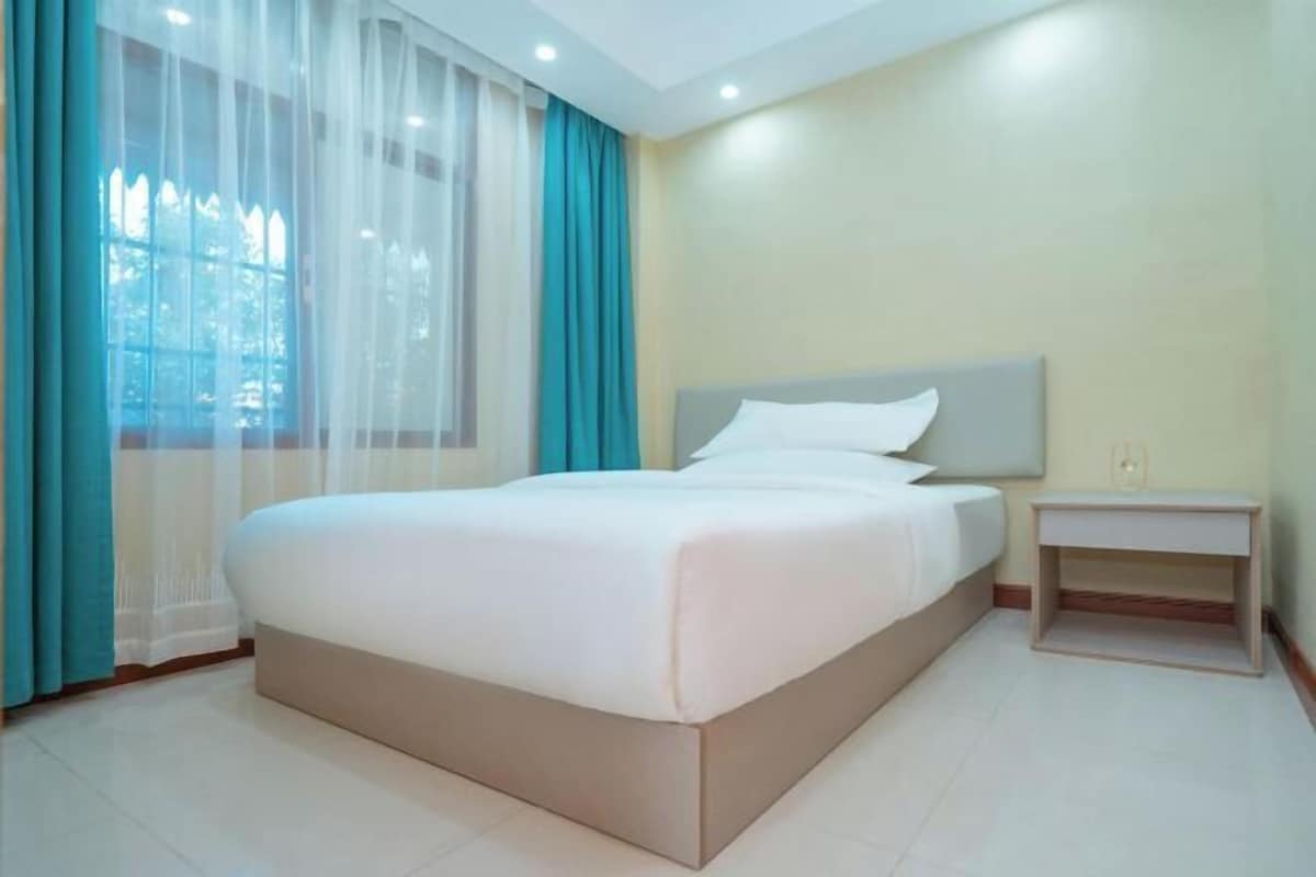 Una habitación de hotel con una cama grande, una mesita de noche y una ventana con cortinas.