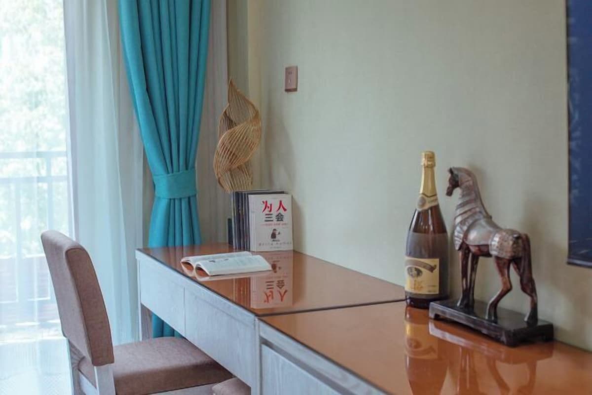 Una habitación de hotel con un escritorio, una silla, una botella de champán, una figura decorativa de un caballo y una lámpara de pared.