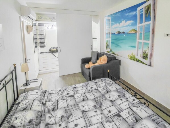 A bedroom with a bed, a sofa, a painting of a beach, and a wardrobe.