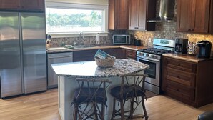 Een moderne keuken met houten kastjes, roestvrijstalen apparatuur, een granieten aanrecht en een centraal kookeiland met barstoelen.