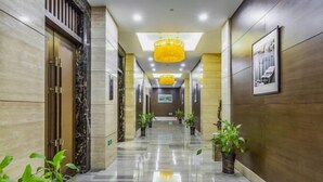 Un pasillo de hotel con suelo de mármol, paredes de madera y arañas de techo amarillas.