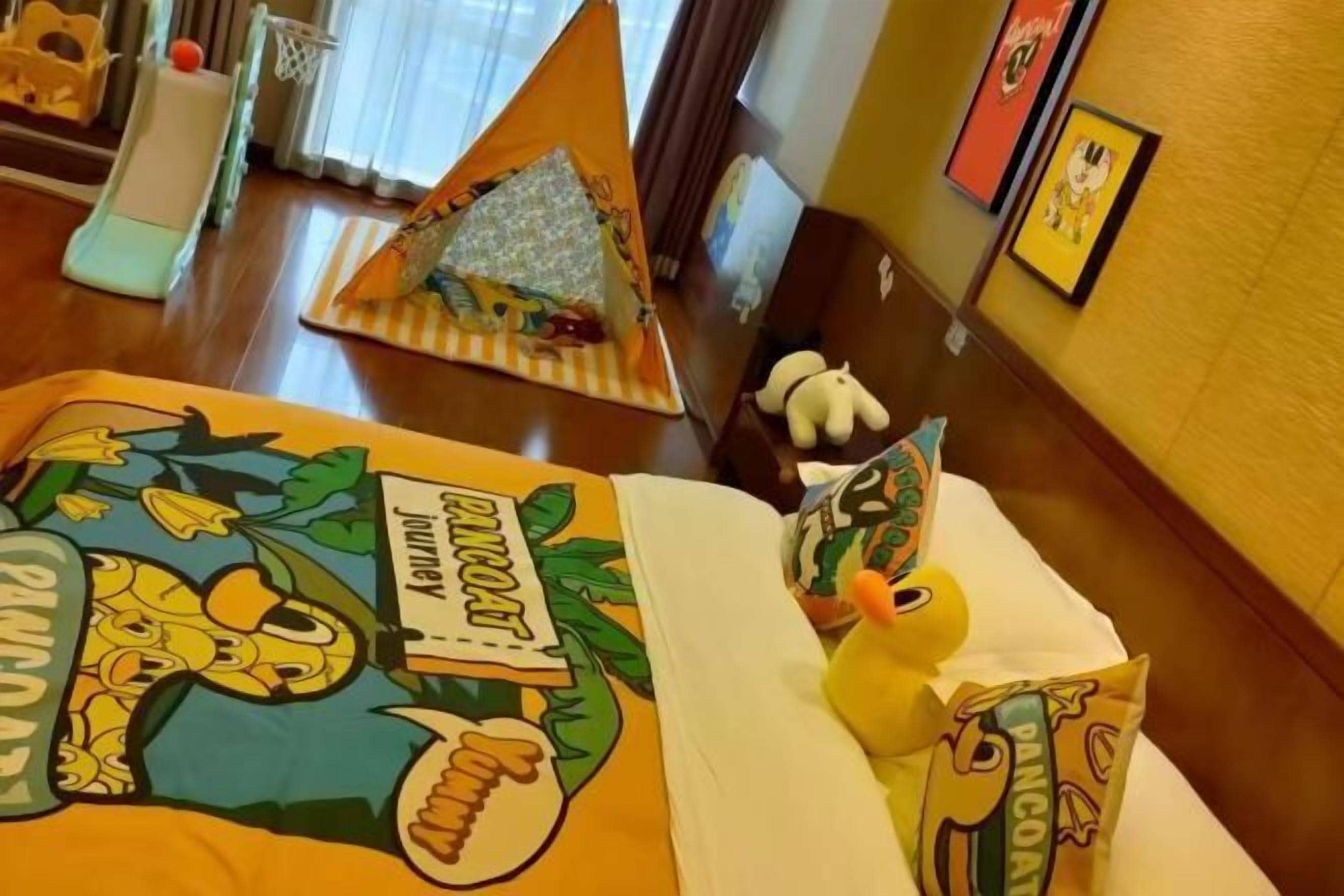 Ein Hotelzimmer mit einem Bett mit Cartoon-Motiv, einer kleinen Spielecke inklusive Spielzeugauto und Ball sowie einem gerahmten Bild an der Wand.