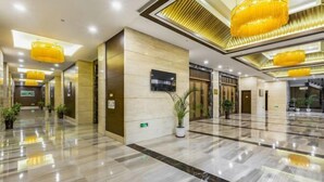 Un vestíbulo amplio con piso de mármol pulido, grandes candelabros amarillos y plantas en macetas.