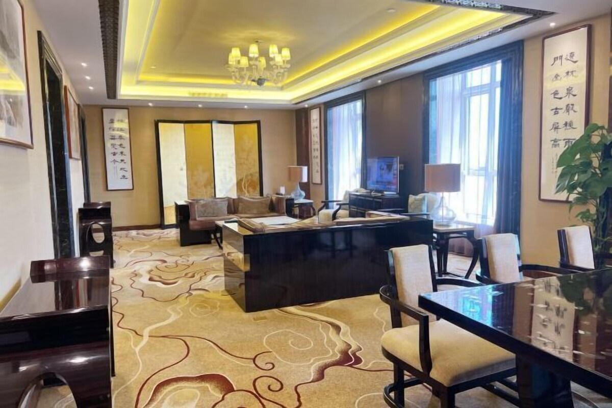 A hotel room with a large bed, a desk, a TV, and a dining area.