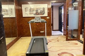 A treadmill in a room with wooden paneling and a patterned carpet. - Xiong'an Meiquan World Holiday hotel (Xiong County)