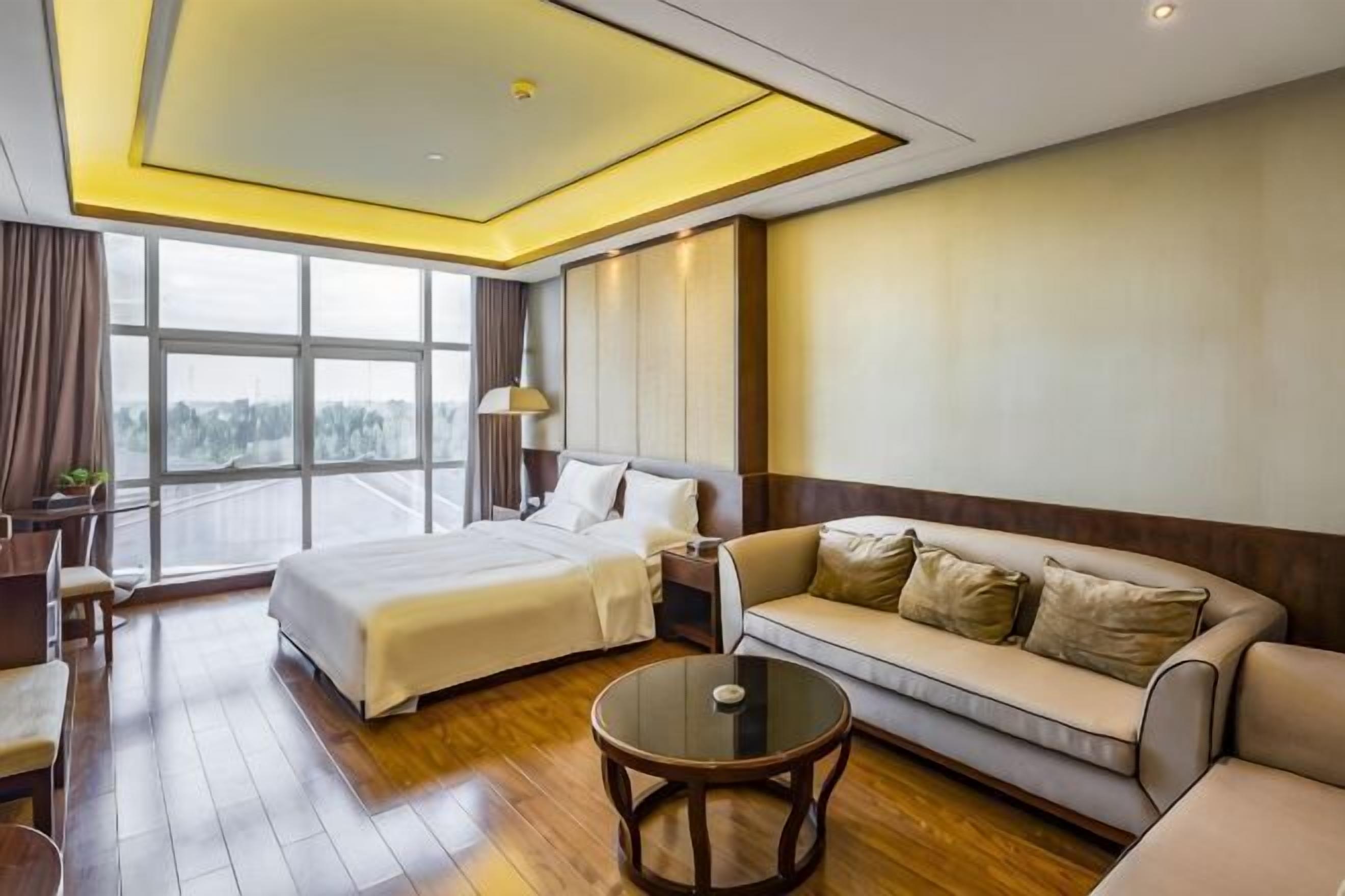A hotel room with a bed, sofa, round coffee table, and a large window.