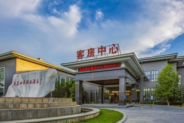 A hotel entrance with a large sign in red characters, a covered walkway, and a landscaped area with a stone sculpture.
