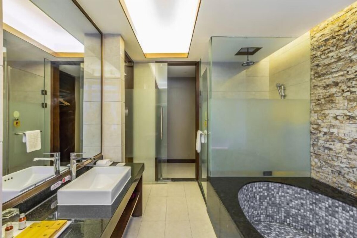 A modern bathroom with a large mirror, two sinks, a shower, and a mosaic-tiled bathtub.