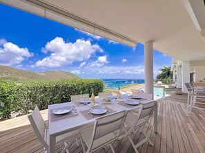 An outdoor dining area with a view of the ocean and hills, equipped with tables and chairs.