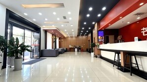 A hotel lobby with a reception desk, seating area, and large windows.