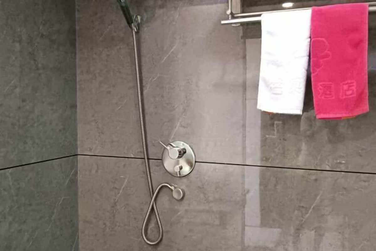 A bathroom with a shower, a towel rack with a white and a pink towel, and a metallic shower control panel.