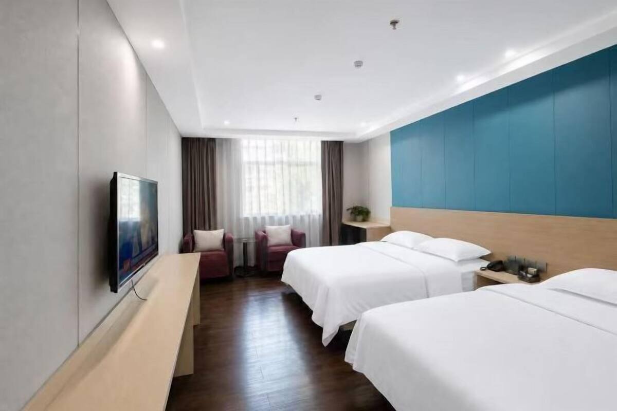 A hotel room with two beds, a TV, a desk, and a window with curtains.
