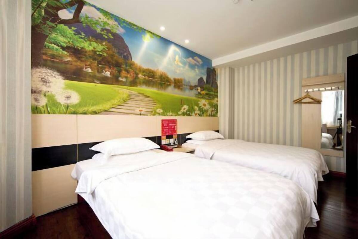 A hotel room with two beds, a large mural on the wall, a mirror, and a striped wall.