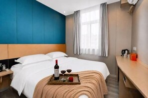 A hotel room with a bed, a bedside table with a bottle and glasses, a tray with a bottle, a red apple, and a blanket.