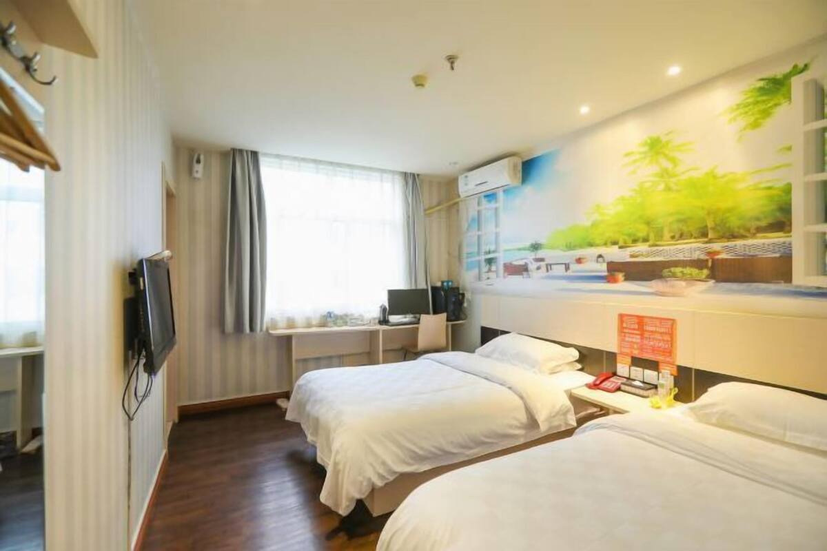 A hotel room with two beds, a desk with a computer, a TV, and a mural of a tropical scene.