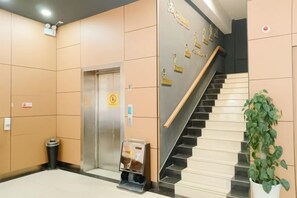 Un vestíbulo de hotel con una escalera, un ascensor y una máquina expendedora.