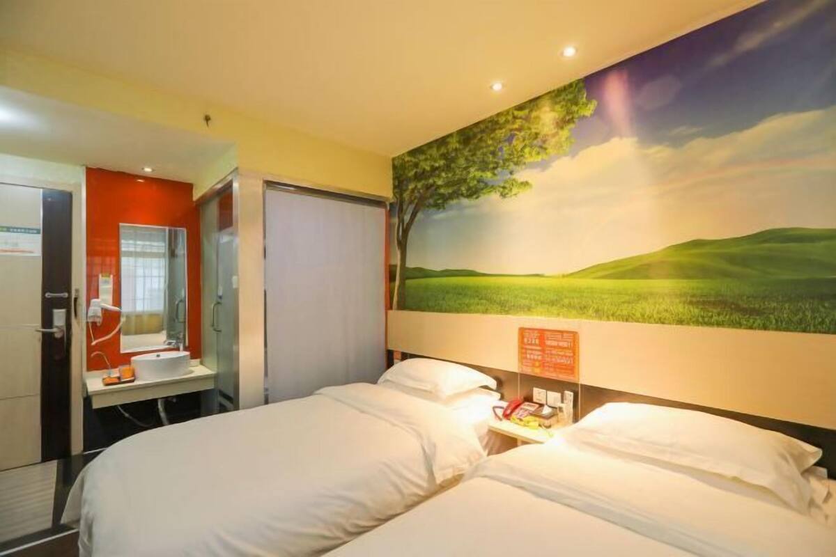 A hotel room with two beds, a bathroom with a mirror and sink, and a mural of a landscape on the wall.