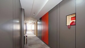 A modern hallway with a metallic floor, a red accent wall, and a mounted phone.