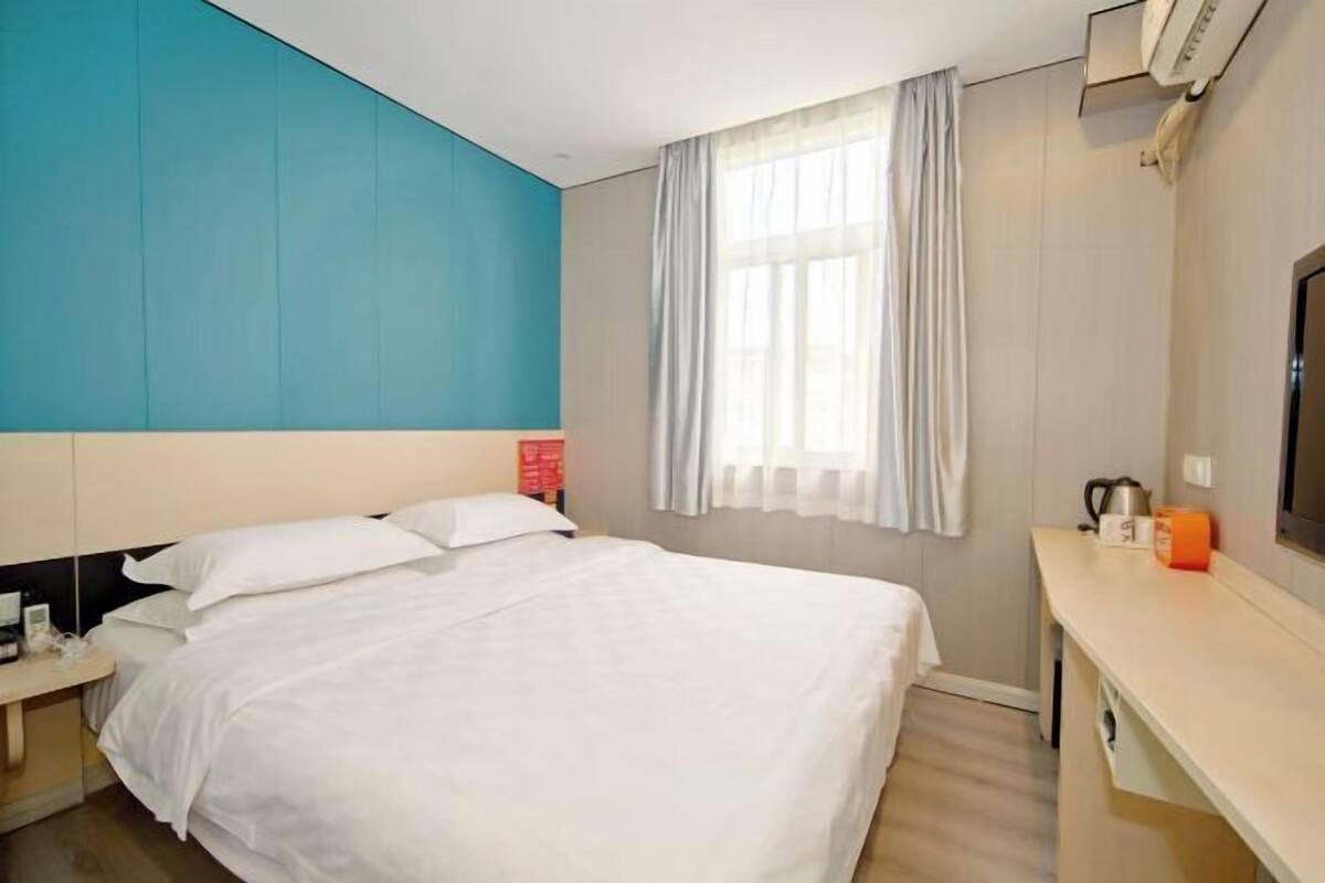 A hotel room with a bed, a desk, a TV, and a window with curtains.