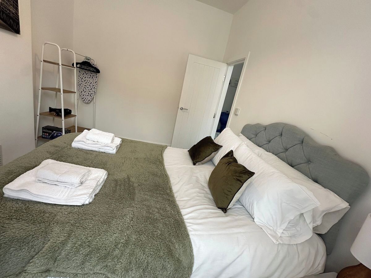 A bedroom with a bed, pillows, a blanket, and a shelf with towels.