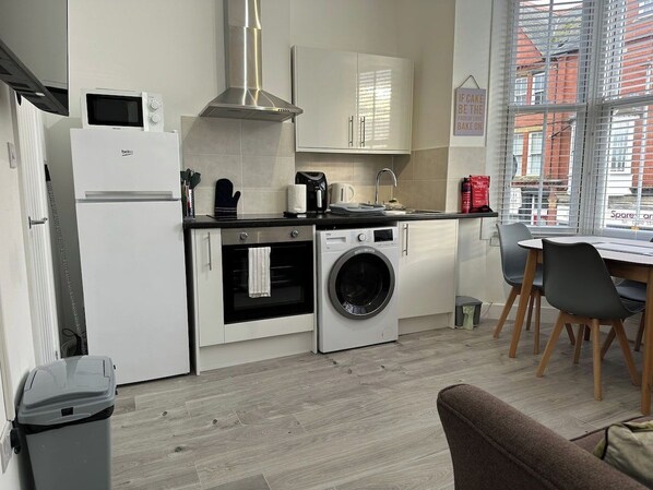 A compact kitchen with a microwave, oven, and washing machine. There is a dining area with a table and chairs.