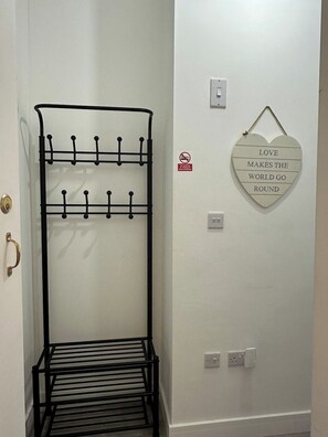 A metal coat rack with hooks, a wall-mounted light switch, a power outlet, and a heart-shaped sign with a love quote.