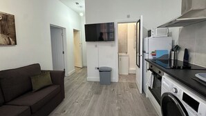Un espace de vie compact comprenant un canapé, un téléviseur, un coin cuisine avec un four à micro-ondes et un lave-linge.