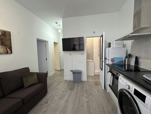 A compact living space with a sofa, a television, a kitchen area with a microwave, and a washing machine.