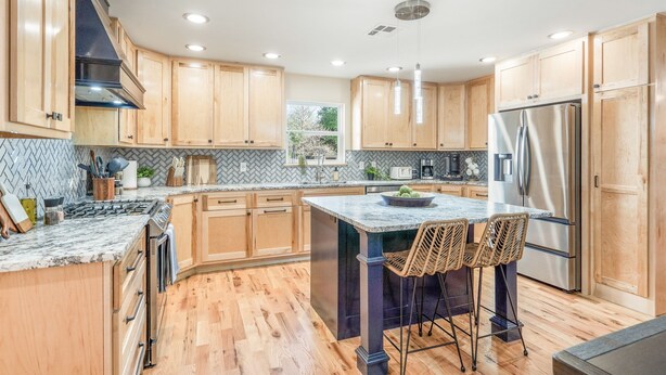 A modern kitchen with wooden cabinets, a central island with bar stools, stainless steel appliances, and a herringbone tile backsplash. - Sleeps 22—Pickleball~Hot Tub~Pool Table~Games (Broken Arrow)