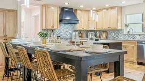 A modern kitchen with a large island, wooden cabinets, and a black range hood. - Sleeps 22—Pickleball~Hot Tub~Pool Table~Games (Broken Arrow)