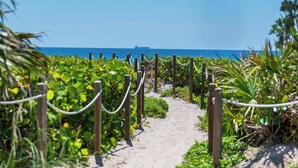 Ein Weg führt zu einem Strand, in der Ferne ein Schiff.
