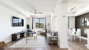 Ein modernes Wohnzimmer mit Sofa, Couchtisch und Fernseher. Es gibt einen Essbereich mit Tisch und Stühlen.