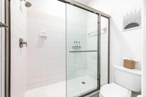 A modern bathroom with a glass-enclosed shower, white tiles, a toilet, and a towel rack. - Renovated Townhome with King & Lakeview (Delray Beach)