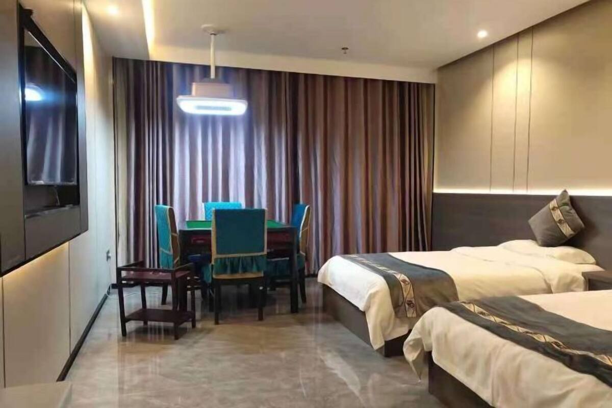 Une chambre d’hôtel avec deux lits, une table à manger avec des chaises, un téléviseur à écran plat et une grande fenêtre avec des rideaux.