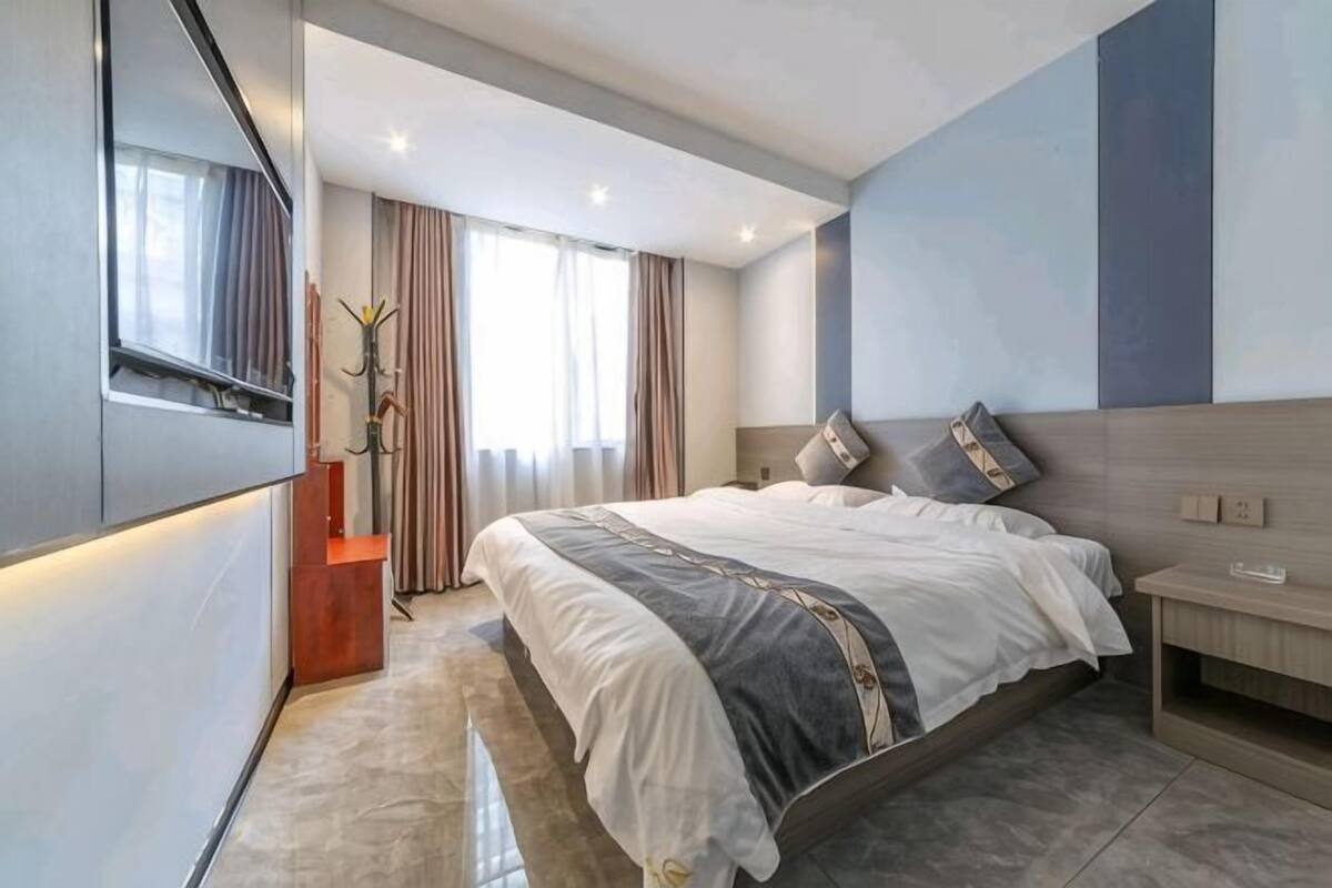 Une chambre d’hôtel moderne avec un grand lit, des tables de chevet, une télévision et une fenêtre avec des rideaux.