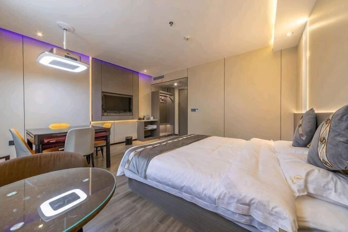 A modern hotel room with a bed, desk, chair, and TV.