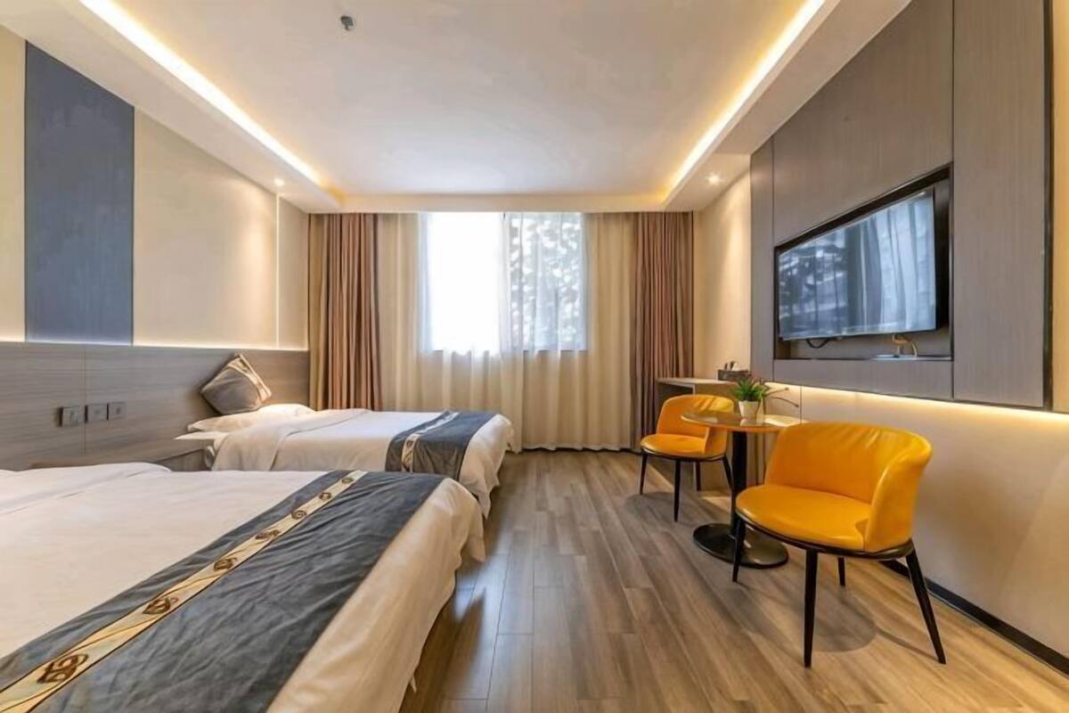 Une chambre d’hôtel avec deux lits, une télévision, une petite table avec une chaise et une fenêtre avec des rideaux.