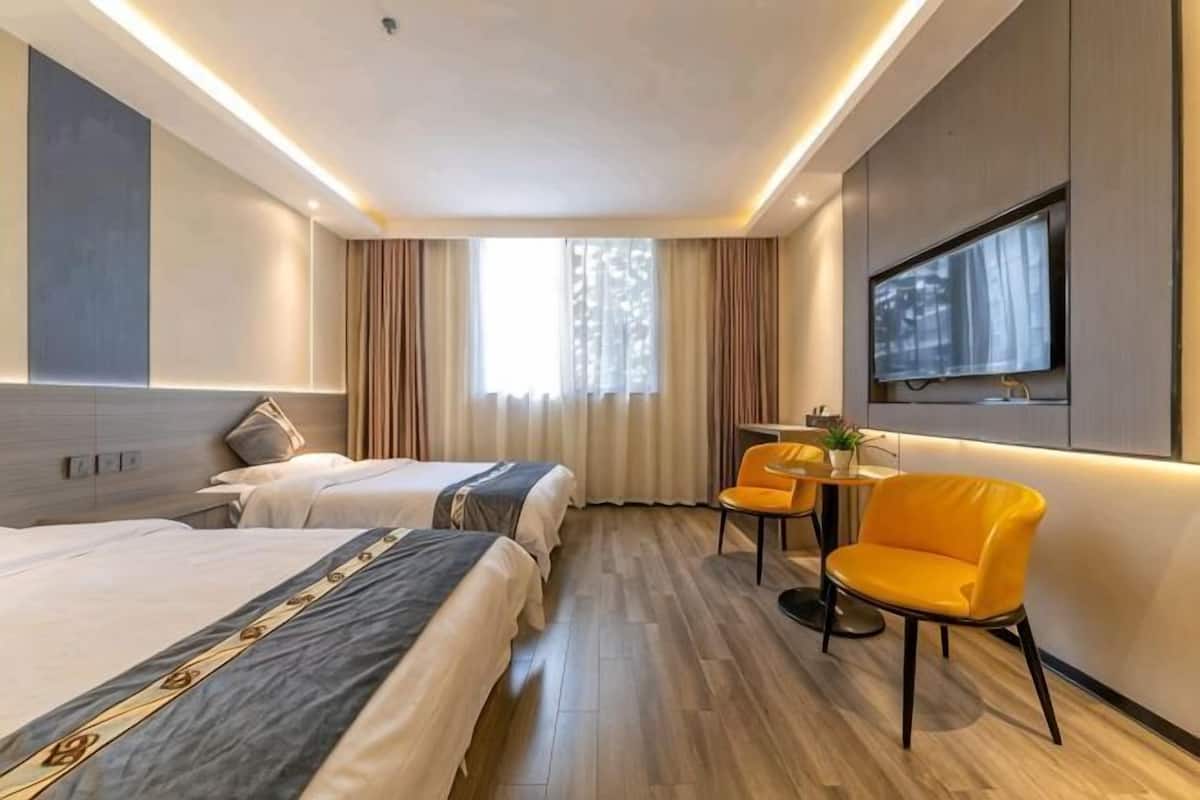 A hotel room with two beds, a TV, a small table with a chair, and a window with curtains.
