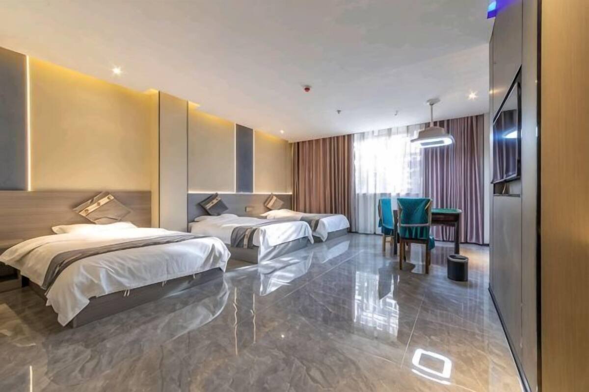 Une chambre d’hôtel moderne équipée de trois lits, d’un coin salon et d’une télévision.