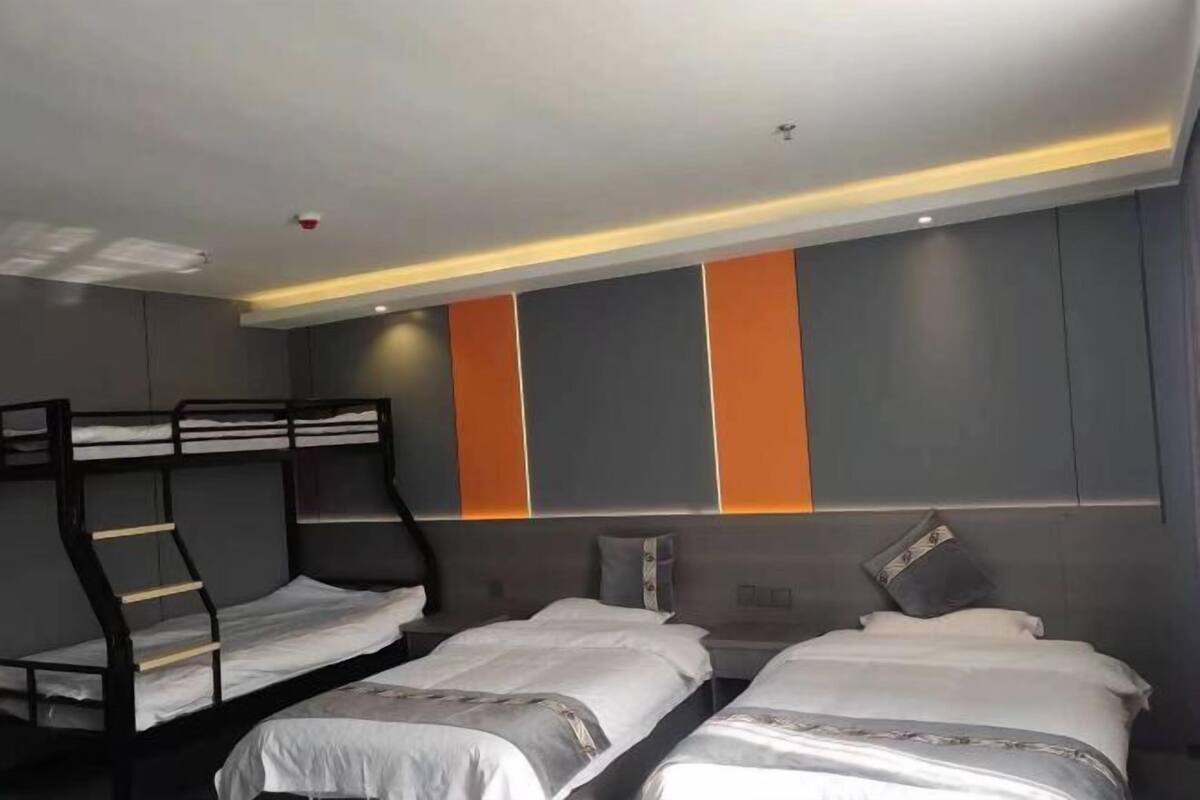 Une chambre d’hôtel avec des lits superposés, un lit et une tête de lit agrémentée de touches de couleur orange.