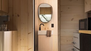 Interior de madera con un espejo redondo sobre un lavamanos, una toalla colgada en la pared y un microondas en un mueble.