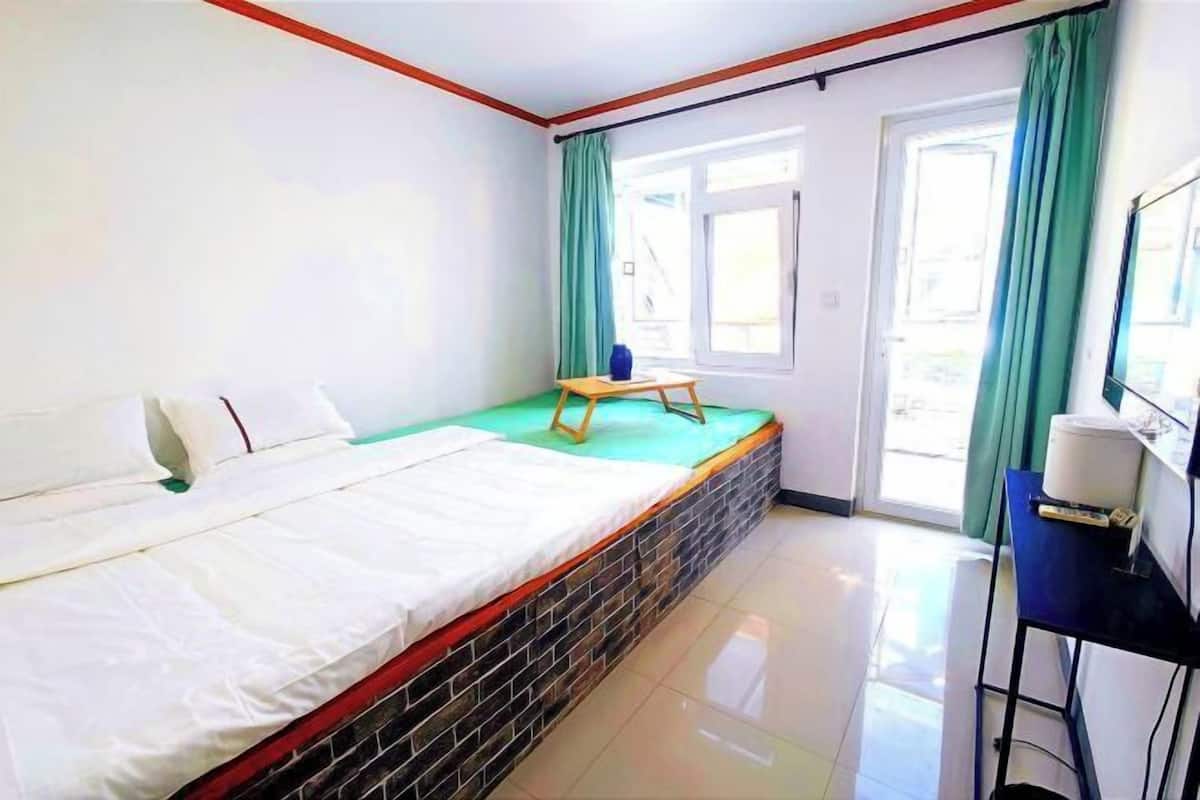 Une pièce comprenant un lit, une petite table, une chaise, une fenêtre avec des rideaux et une porte.