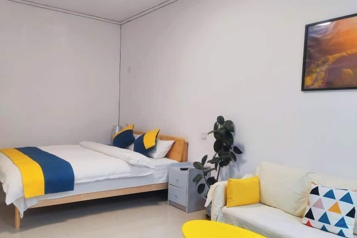 Une chambre moderne avec un lit, une table de chevet, un canapé et une plante fixée au mur.