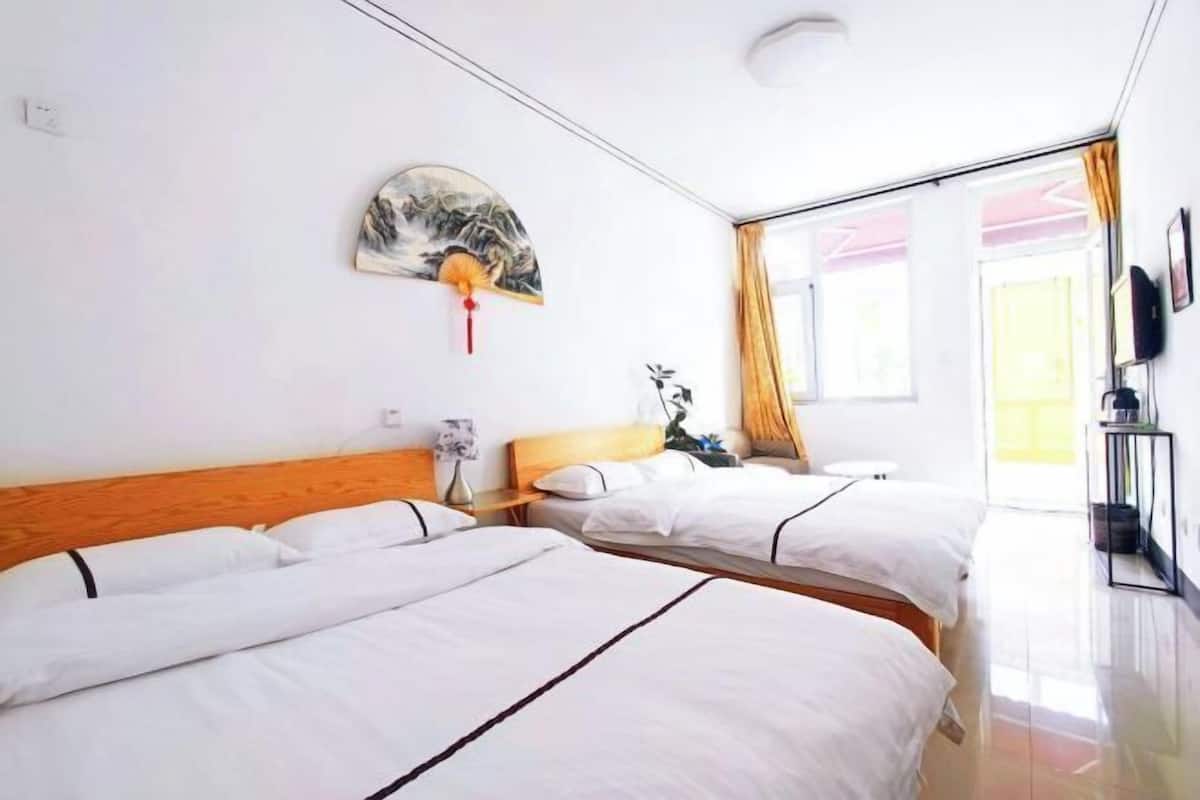 Une chambre d’hôtel avec deux lits, un tableau au mur, une plante et une fenêtre avec des rideaux.