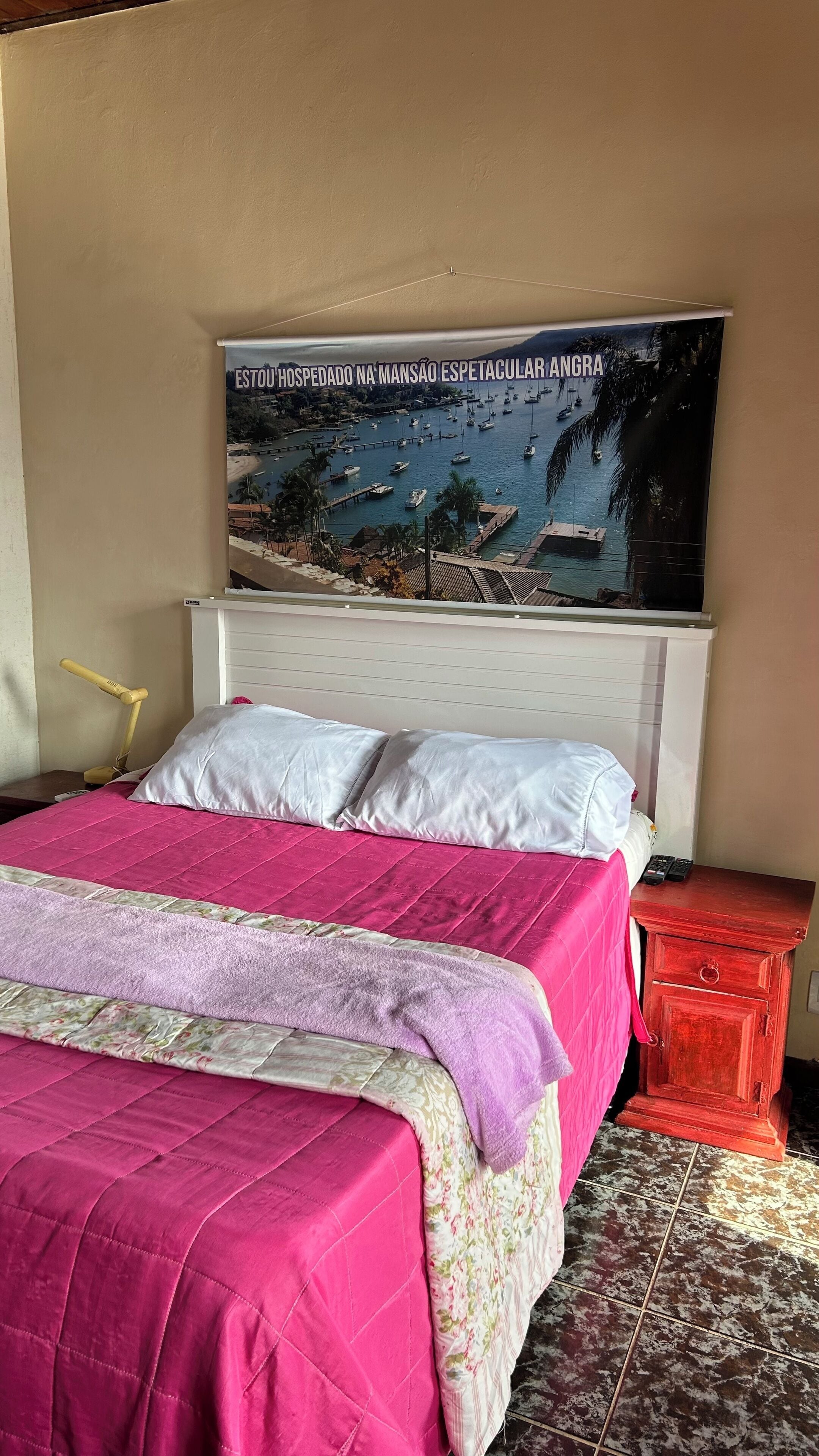 Ein Schlafzimmer mit einem Bett, einem Nachttisch, einer Lampe und einem Poster an der Wand.