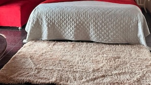 Quarto com cama, sofá vermelho, tapete fofo e teto de madeira.